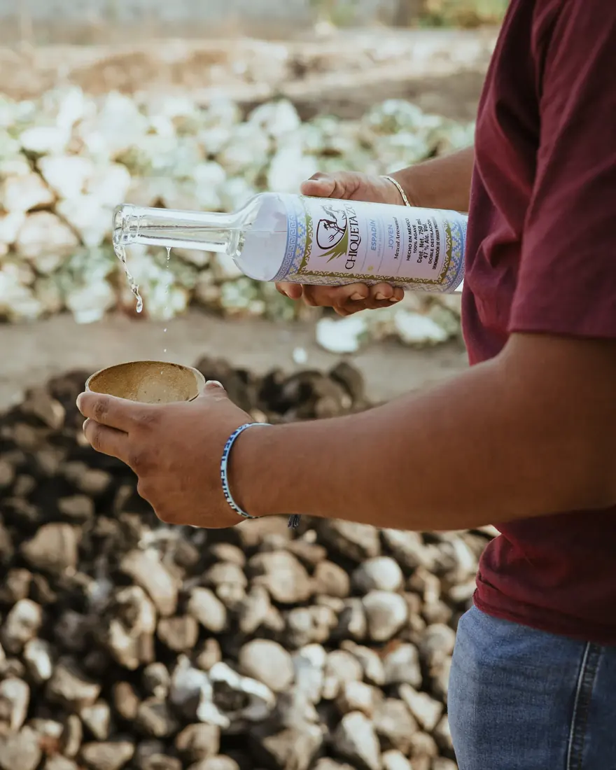 Alguien sirve mezcal de una botella de Chiquetazo Espadín en una jícara pequeña, al aire libre.